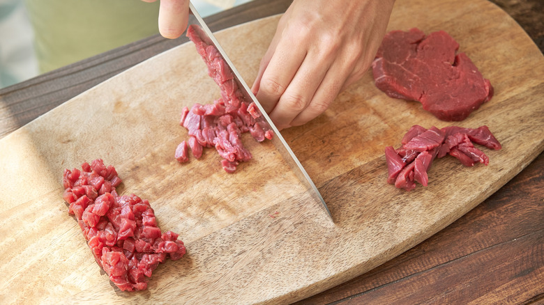 Hands finely chopping steak on cutting board