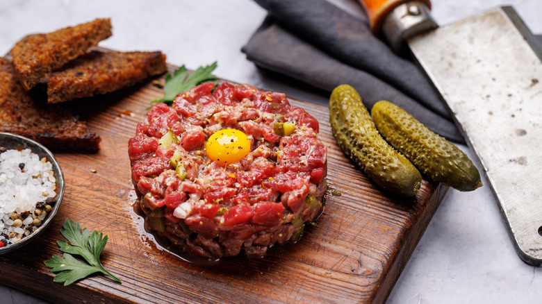 Steak tartare on board with toast, pickles, salt, and an egg yolk