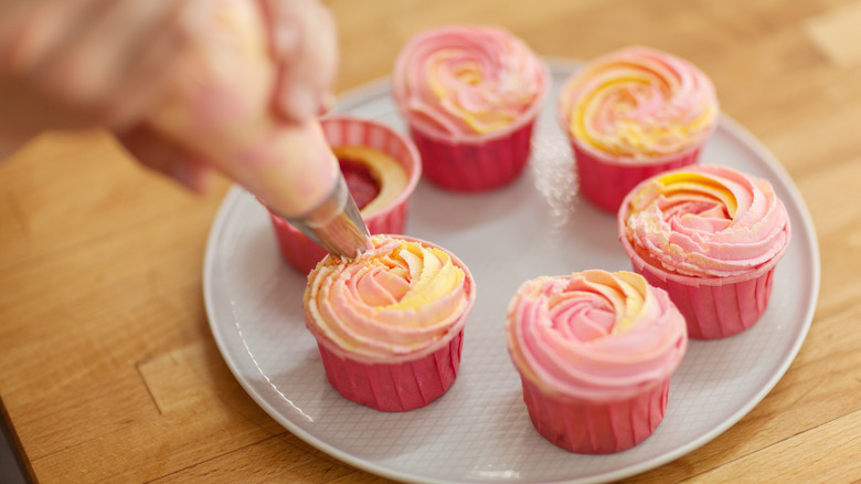 Using a piping bag to frost pink cupcakes on a platter