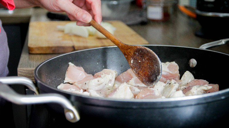 Cooking chicken in a skillet with a wooden spoon