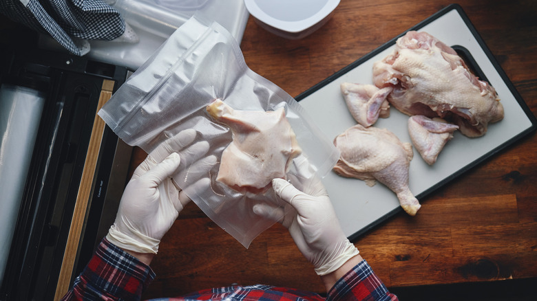 Someone wearing gloves and holding a vacuum sealed piece of raw chicken