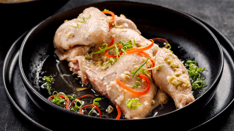 Sous vide chicken with a few garnishes and herbs in a black dish