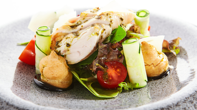 Sous vide chicken with lettuce, tomatoes, rolled up cucumbers, and profiteroles on a small plate