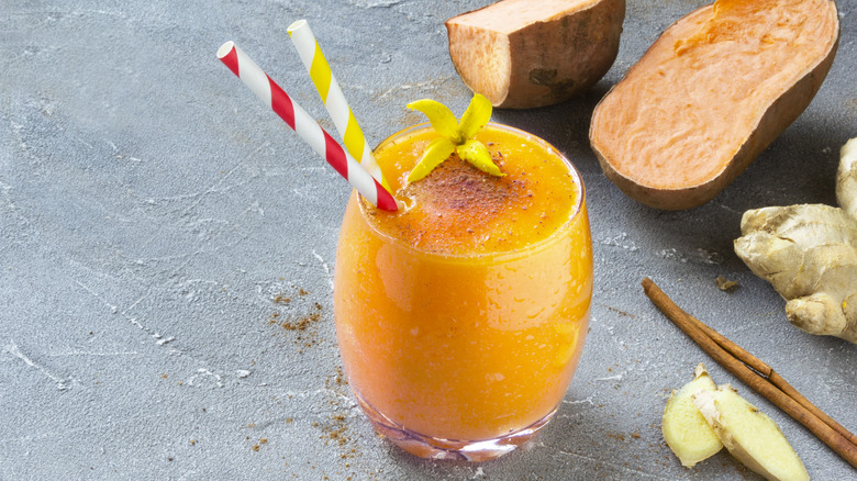 a glass of sweet potato juice next to raw sweet potatoes