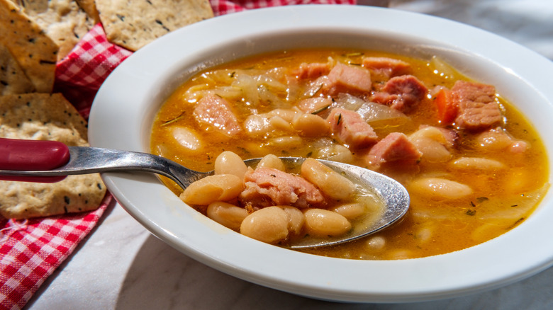 A bowl of bean and ham soup with a spoon in it