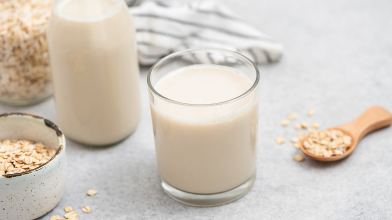 Oat milk in a glass with a containers holding oats next to it.