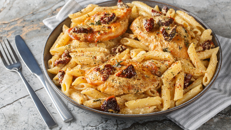 A plate of Marry Me Chicken with a fork and knife next to it.