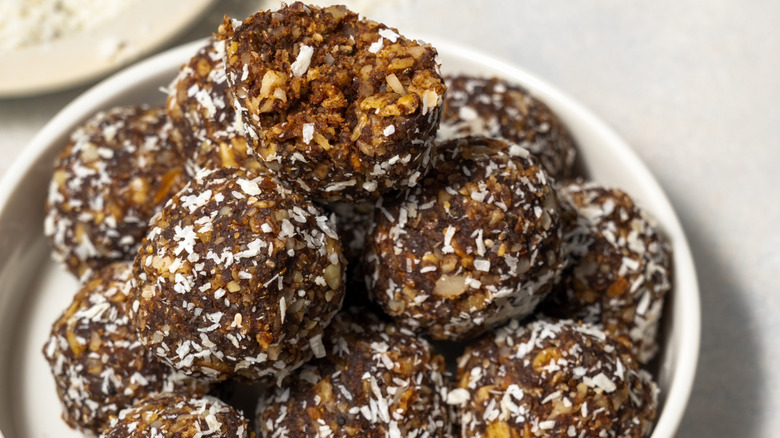 Protein packed energy balls rolled in shredded coconut in a white bowl on a white countertop.