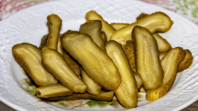 Sliced up pickles on top of a white plate outside.