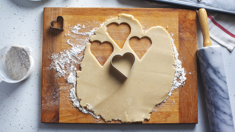 Cookie dough rolled out on a wooden board with heart shaped cookies cut out of it