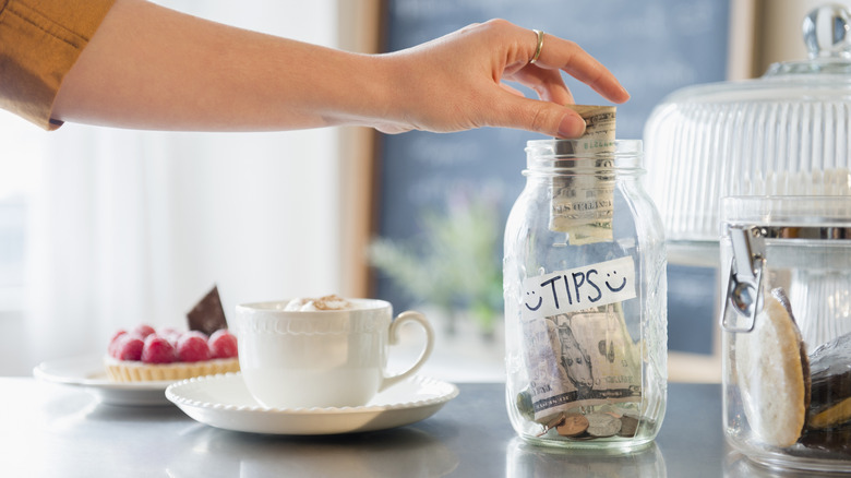 A hand placing money in tip jar