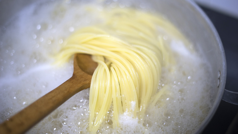 A pot of boiling spaghetti with a wooden spoon lifting some noodles