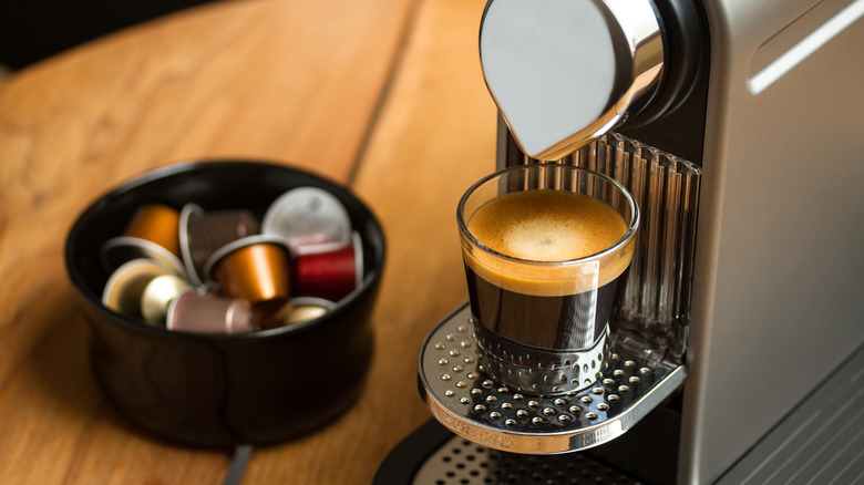 cup of espresso brewed by Nespresso maker next to pods