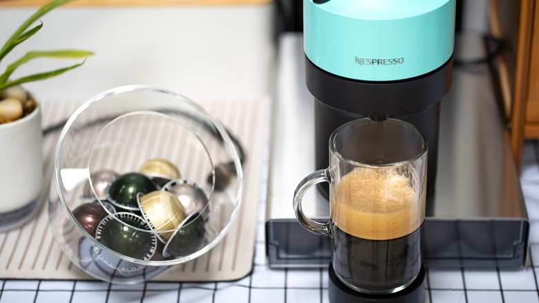 Nespresso machine with a cup of coffee next to pods.