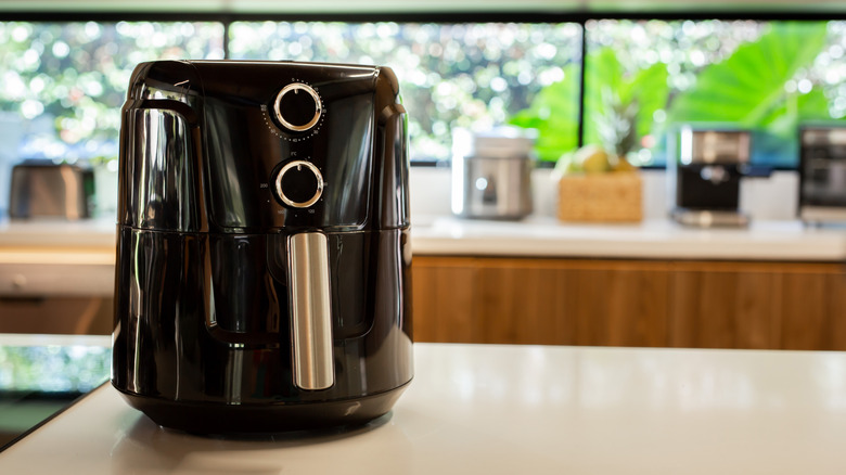 A black air fryer sitting on the table counter with other appliances in the background