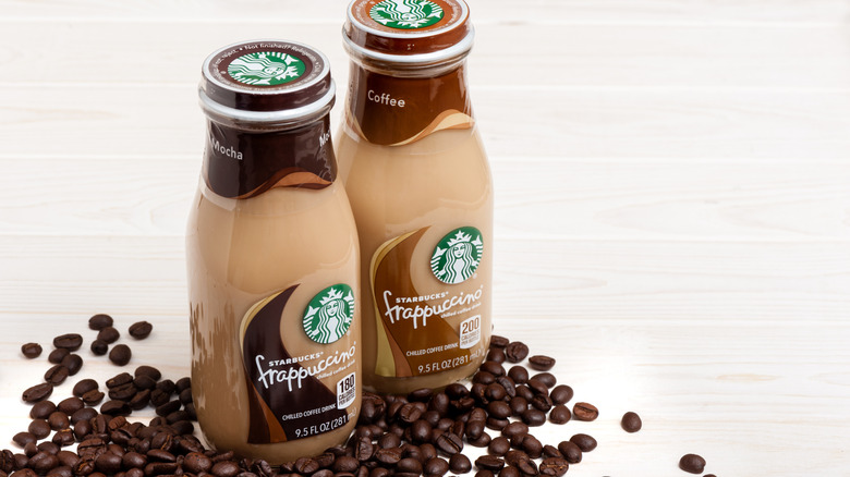 Two bottles of Starbucks Frappuccinos on top of coffee beans on a white surface