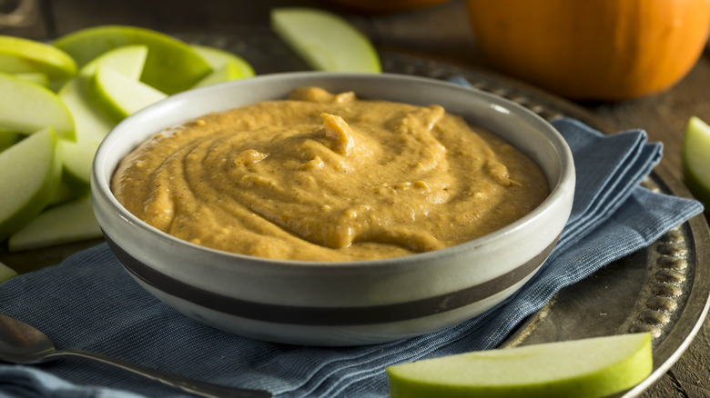 Bowl of pumpkin hummus with green sliced apples on side