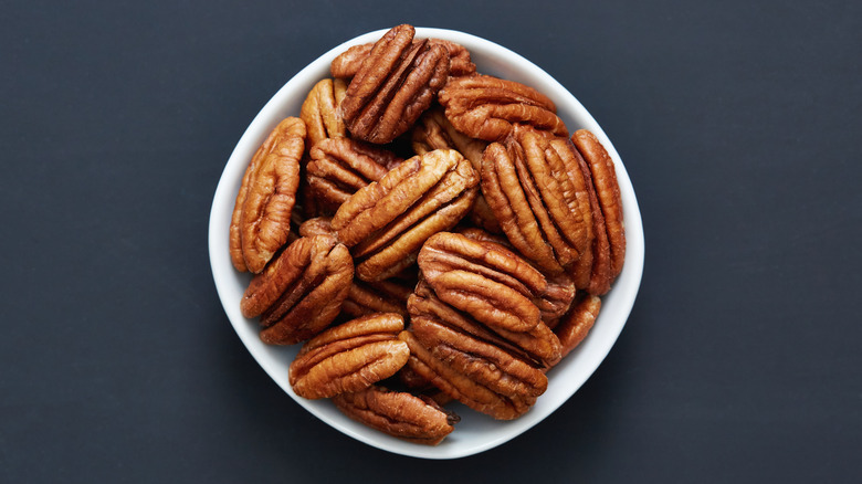 A bowl of toasted pecans on grey background