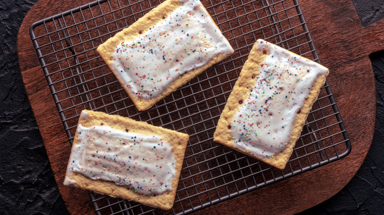 three pop-tarts on a baking rack set on a wooden cutting board