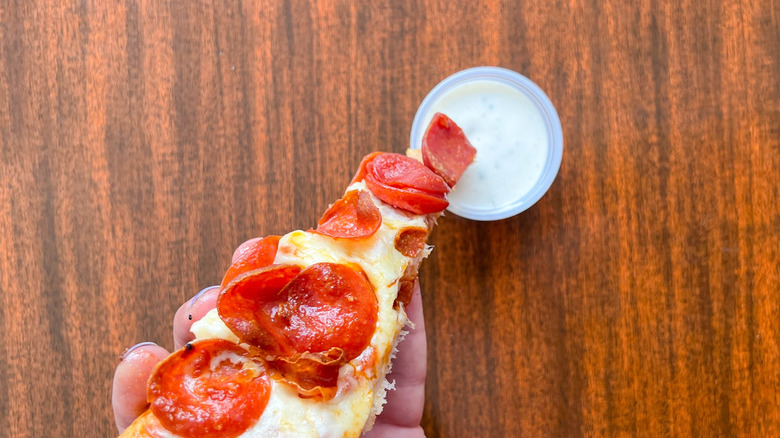 A slice of pepperoni pizza being dipped into ranch dressing