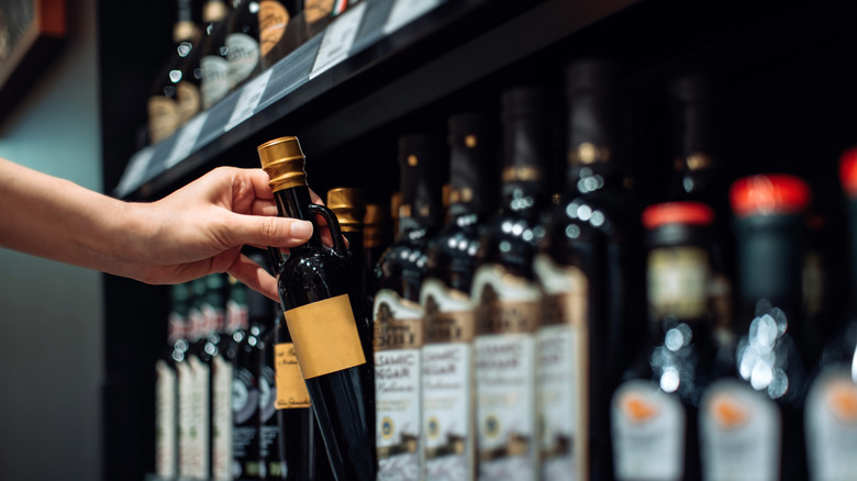 A hand reaching for a bottle of balsamic vinegar on a grocery store shelf