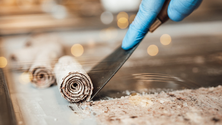 A person wearing blue gloves and making rolled ice cream