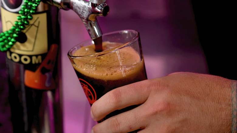 draft beer pouring into a pint glass held by a man's hand