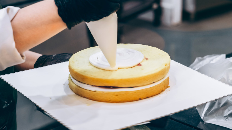 A baker piping icing onto a layer cake