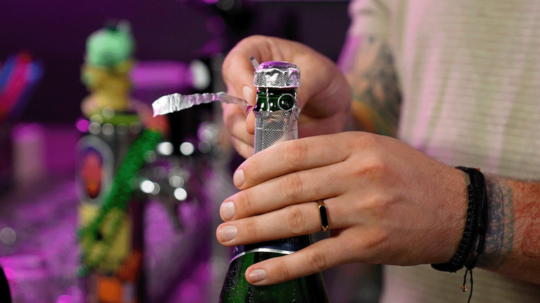 Bartender Kameron Lockwood removes foil from a champagne bottle.